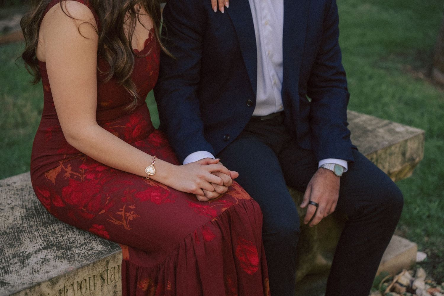 Close-up view of couple sitting together on stone steps, with burgundy dress and navy suit details visible.