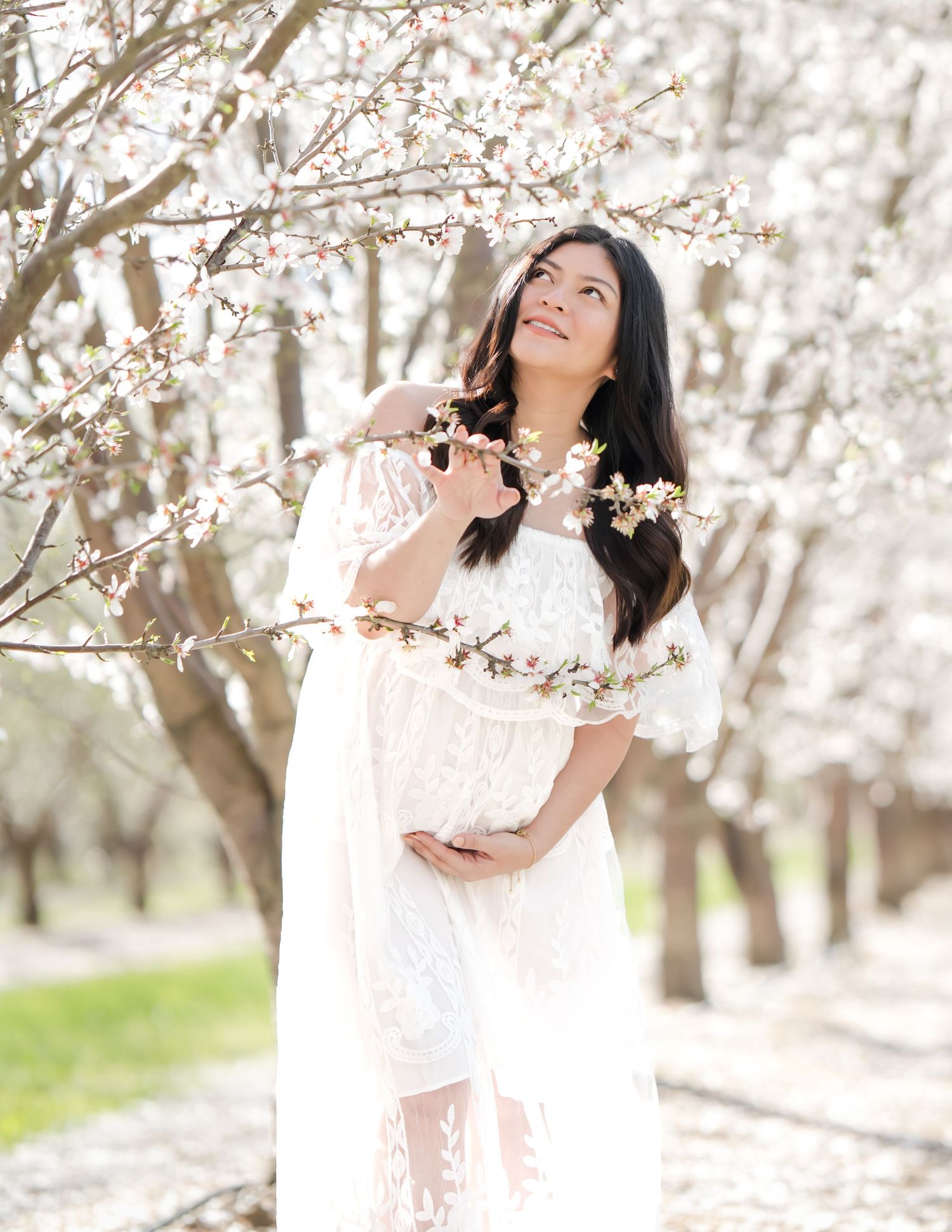 Pregnant woman wearing a flowing dress, standing amidst a sea of pink cherry blossoms, capturing the elegance and serenity of maternity in R