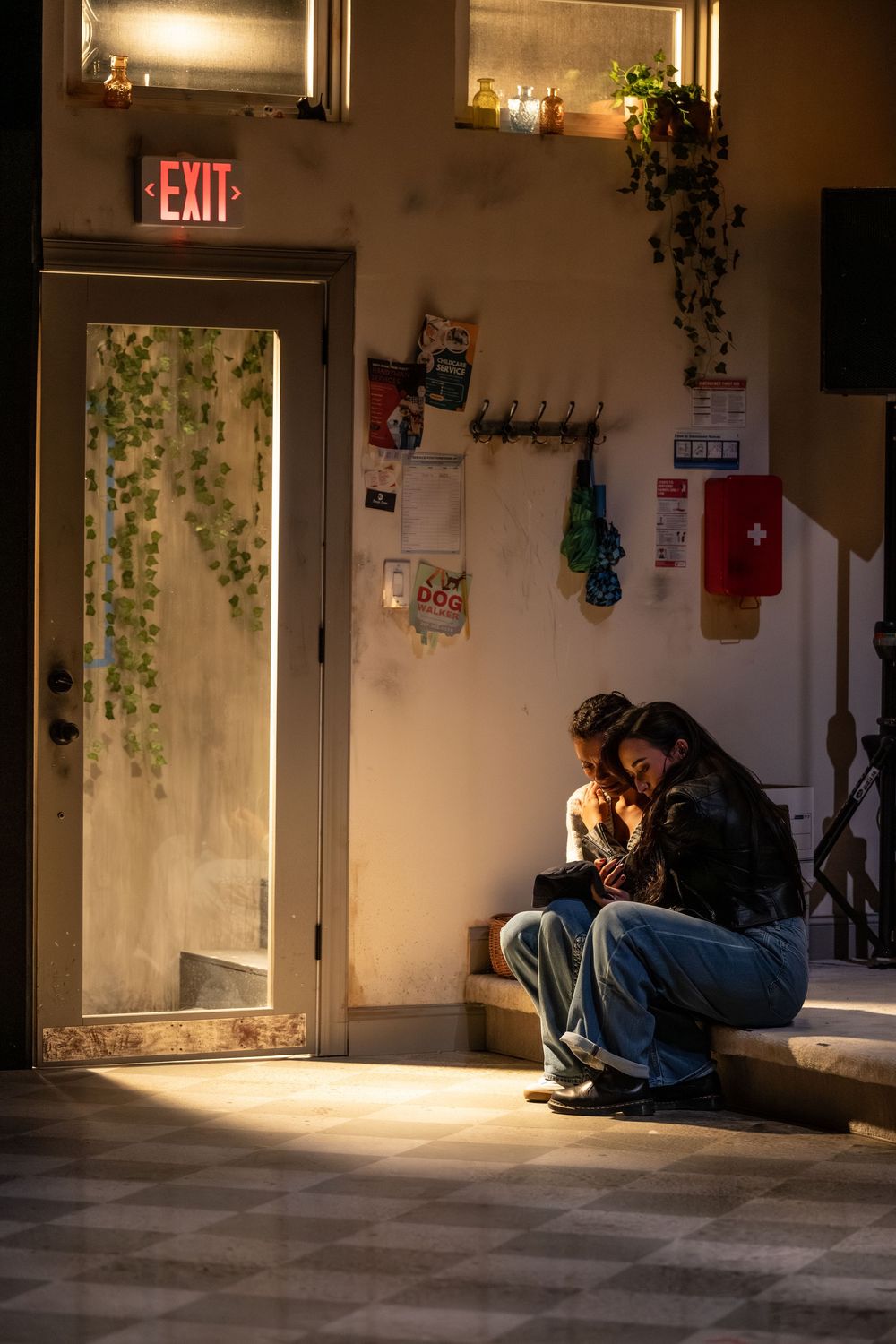 People sitting in a dimly lit room with dramatic sunlight streaming through a window and exit sign visible.