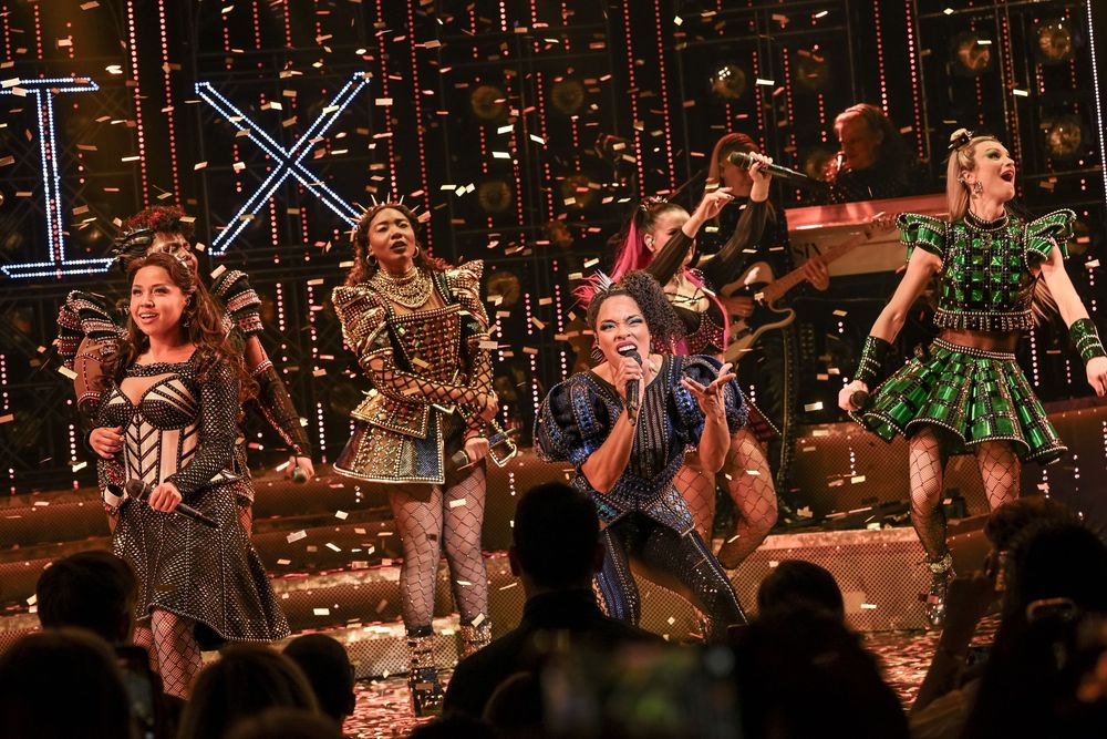 Performers celebrate on stage with confetti falling during a vibrant musical theater production finale.