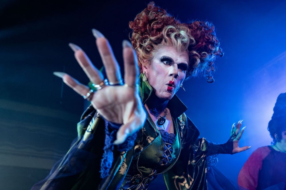 Theatrical performer in dramatic lighting with blue backdrop and expressive movements.