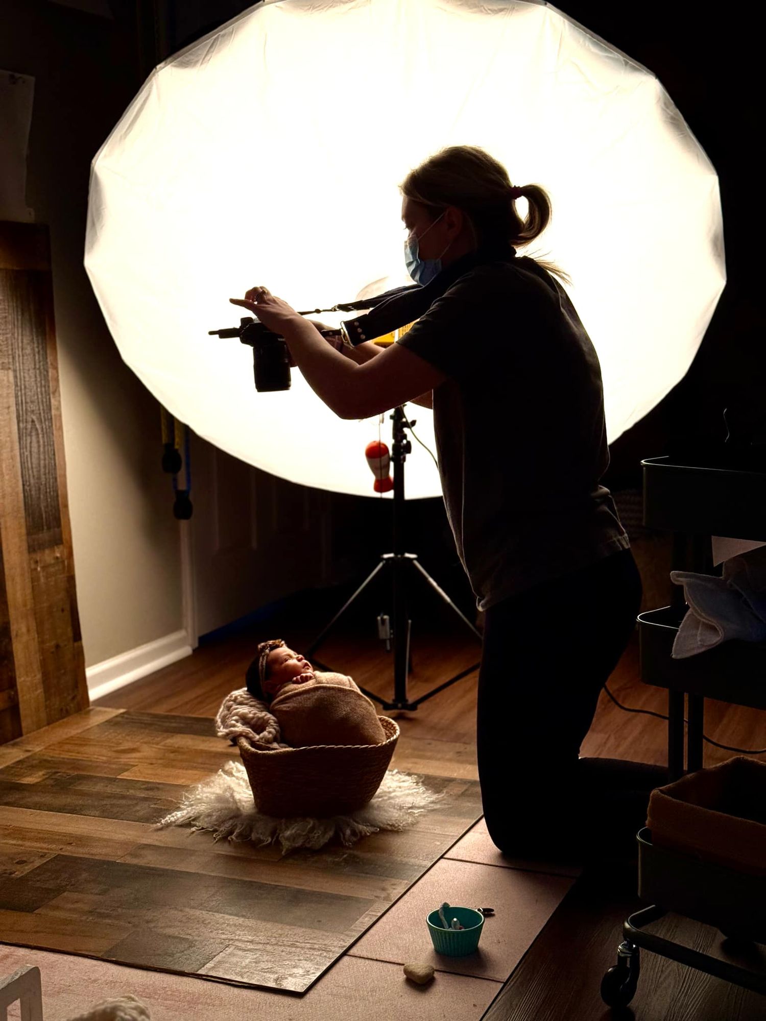 Photographer silhouetted against large softbox light photographing newborn baby in studio.