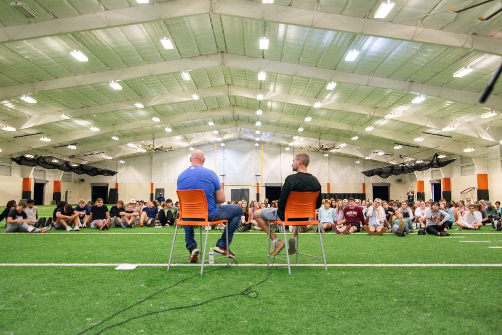 Wide view of an indoor sports facility with green turf and bright overhead lighting.
