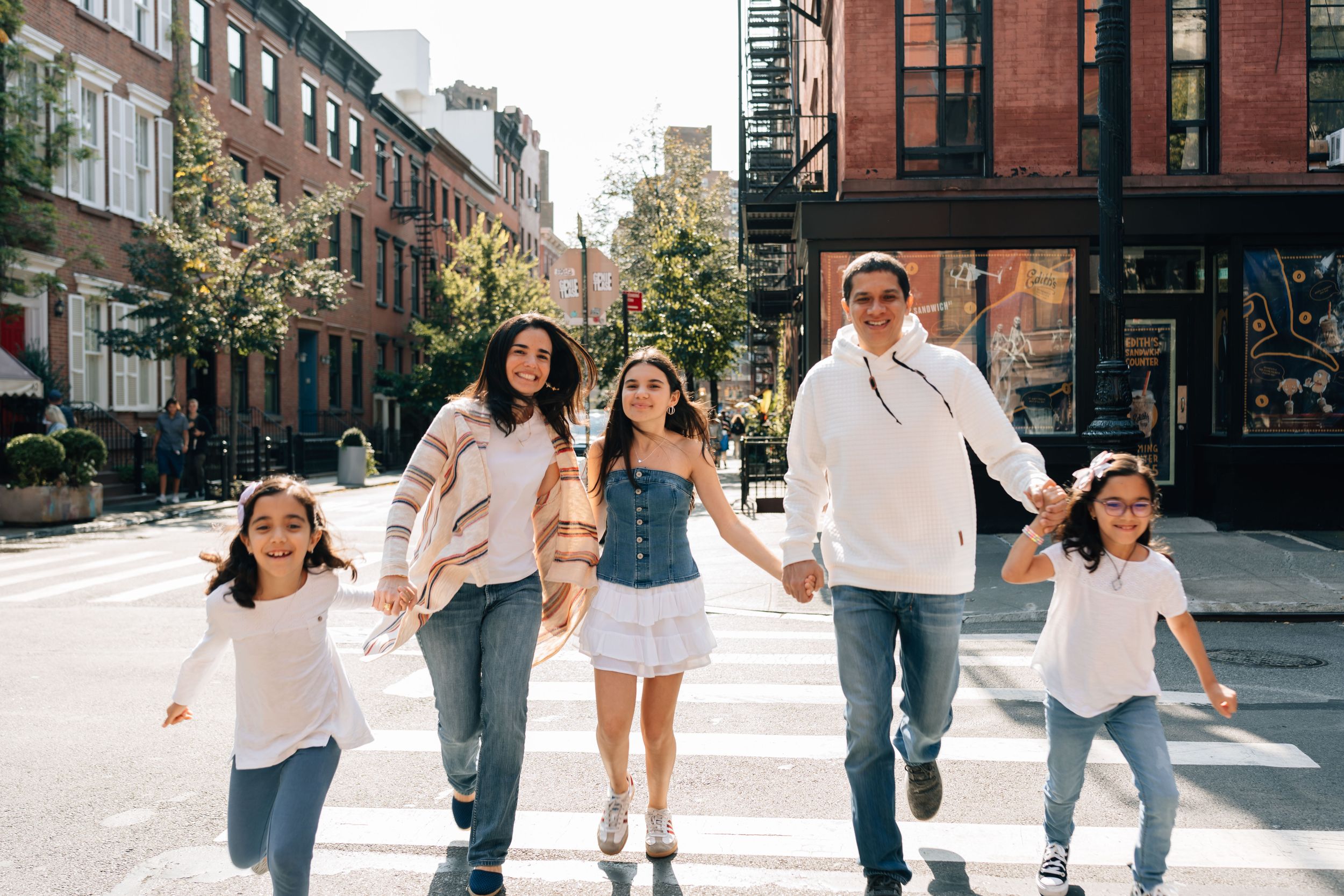 People holding hands while crossing a sunny street in a charming urban neighborhood with brick buildings.