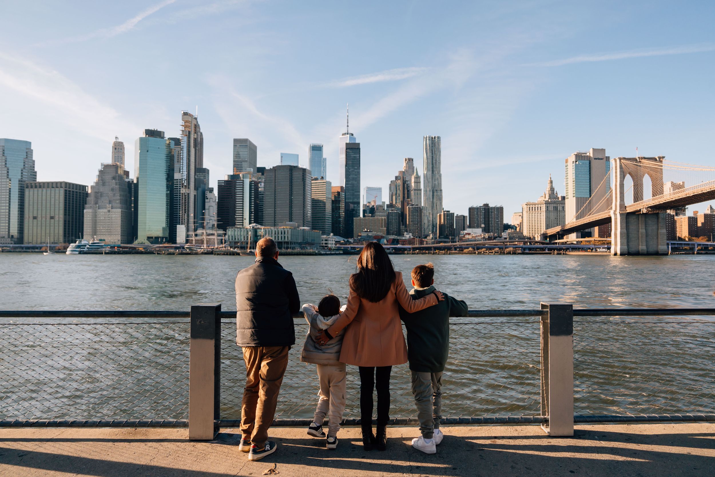 Three people standing at the waterfront overlooking the Manhattan skyline and Brooklyn Bridge in New York City.