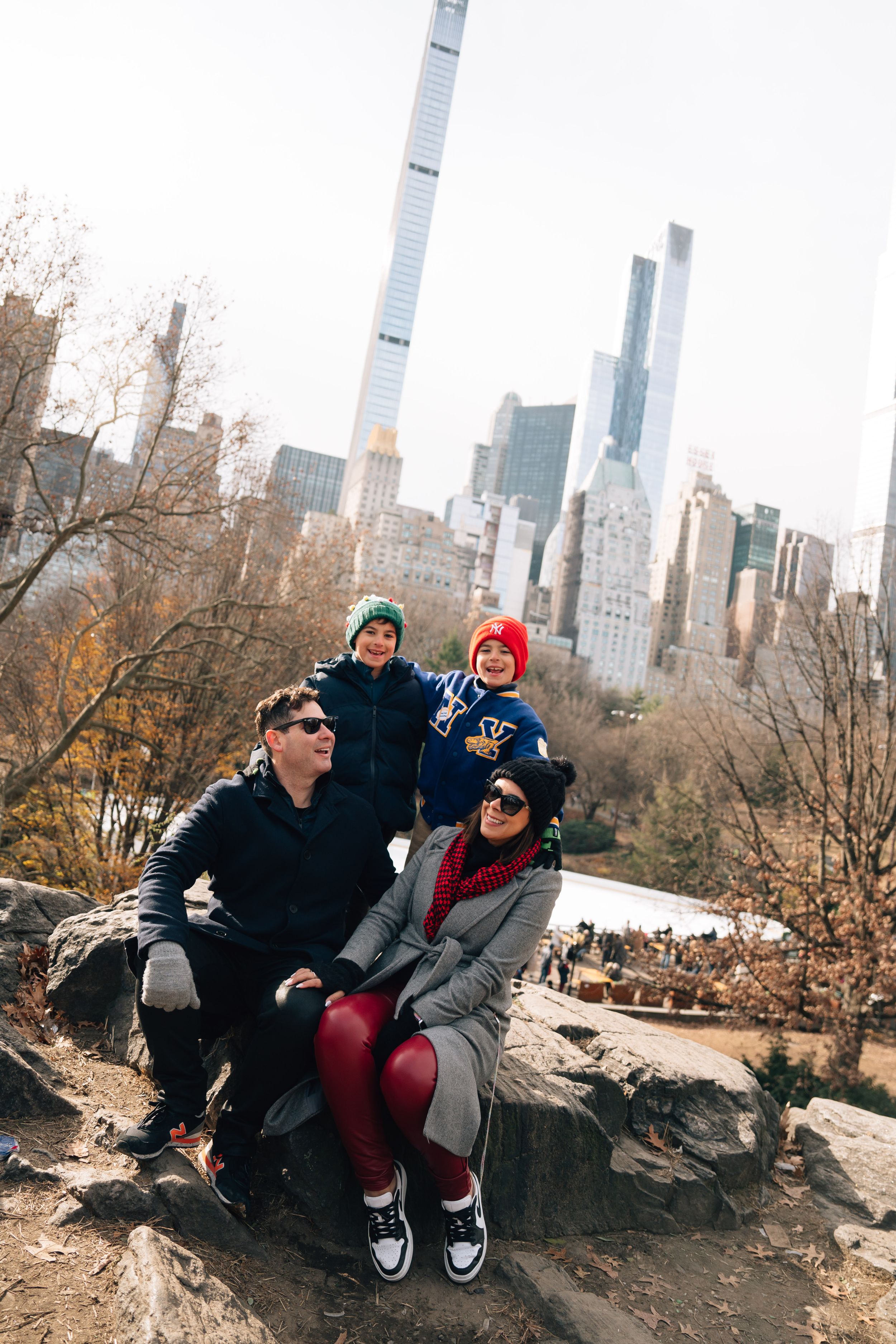 Group sitting on rocks in Central Park on a sunny autumn day with Manhattan skyscrapers towering in the background.