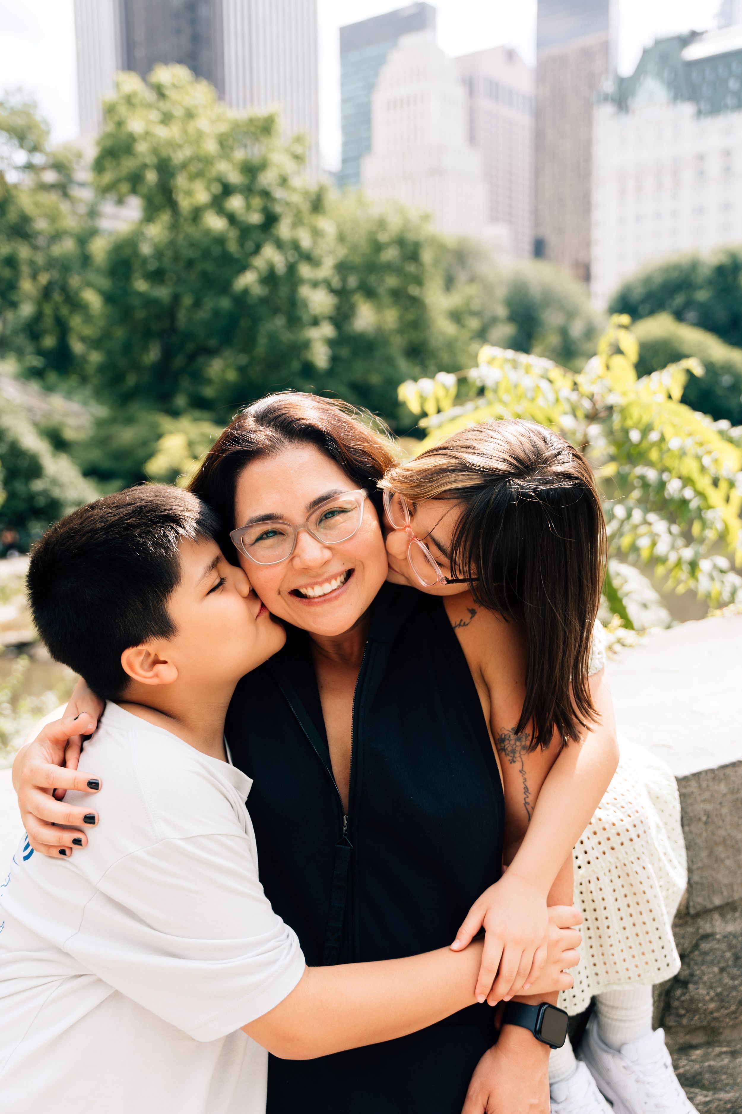 A joyful family moment captured in Central Park with New York City buildings visible in the background.