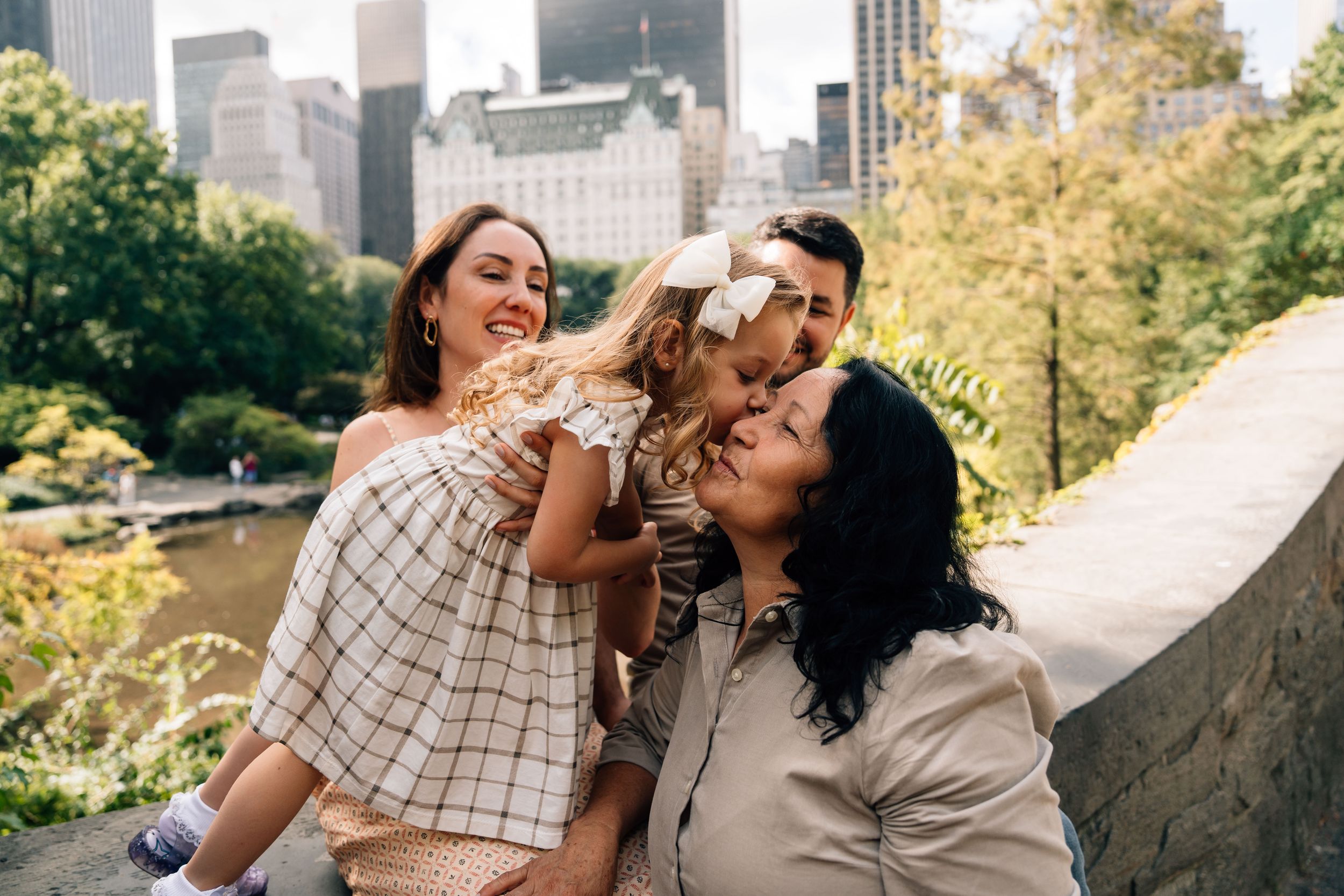 Cheerful people with a small dog enjoy a sunny afternoon in Central Park with Manhattan buildings in the background.