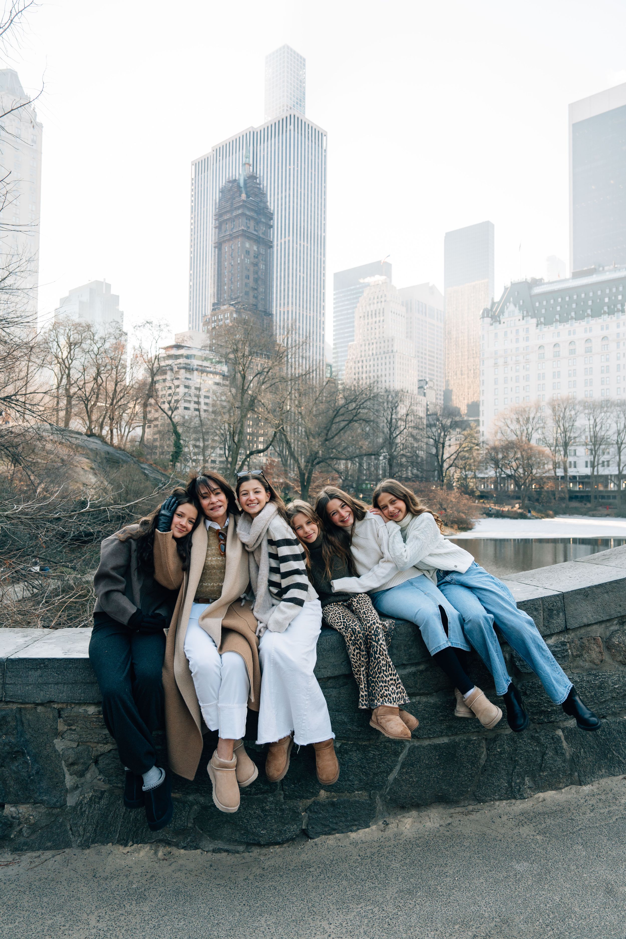 A group of friends sitting together on a wall in Central Park with the NYC skyline and skyscrapers visible in the background.