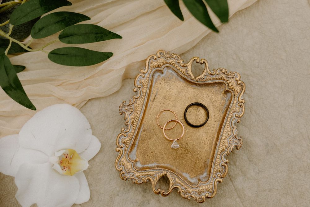 Gold ornate ring dish with wedding bands and white orchid on marble.