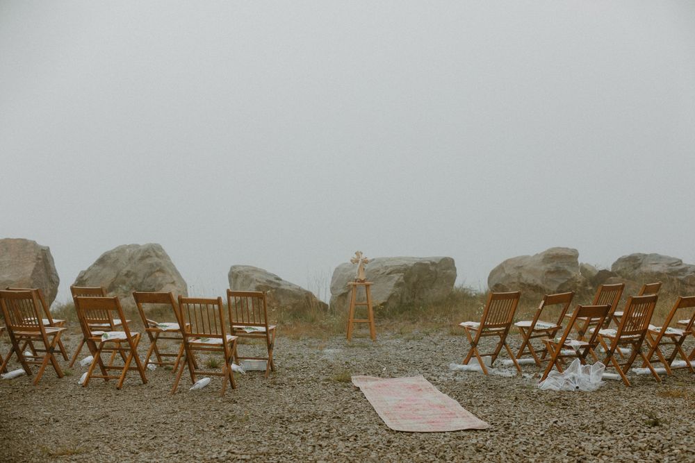 Outdoor wedding ceremony setup with wooden chairs and large rocks in fog.