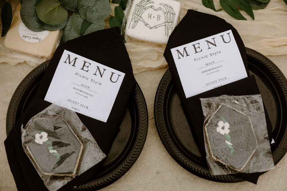 Elegant wedding place settings with black napkins, menu cards, and floral cookies on dark charger plates.