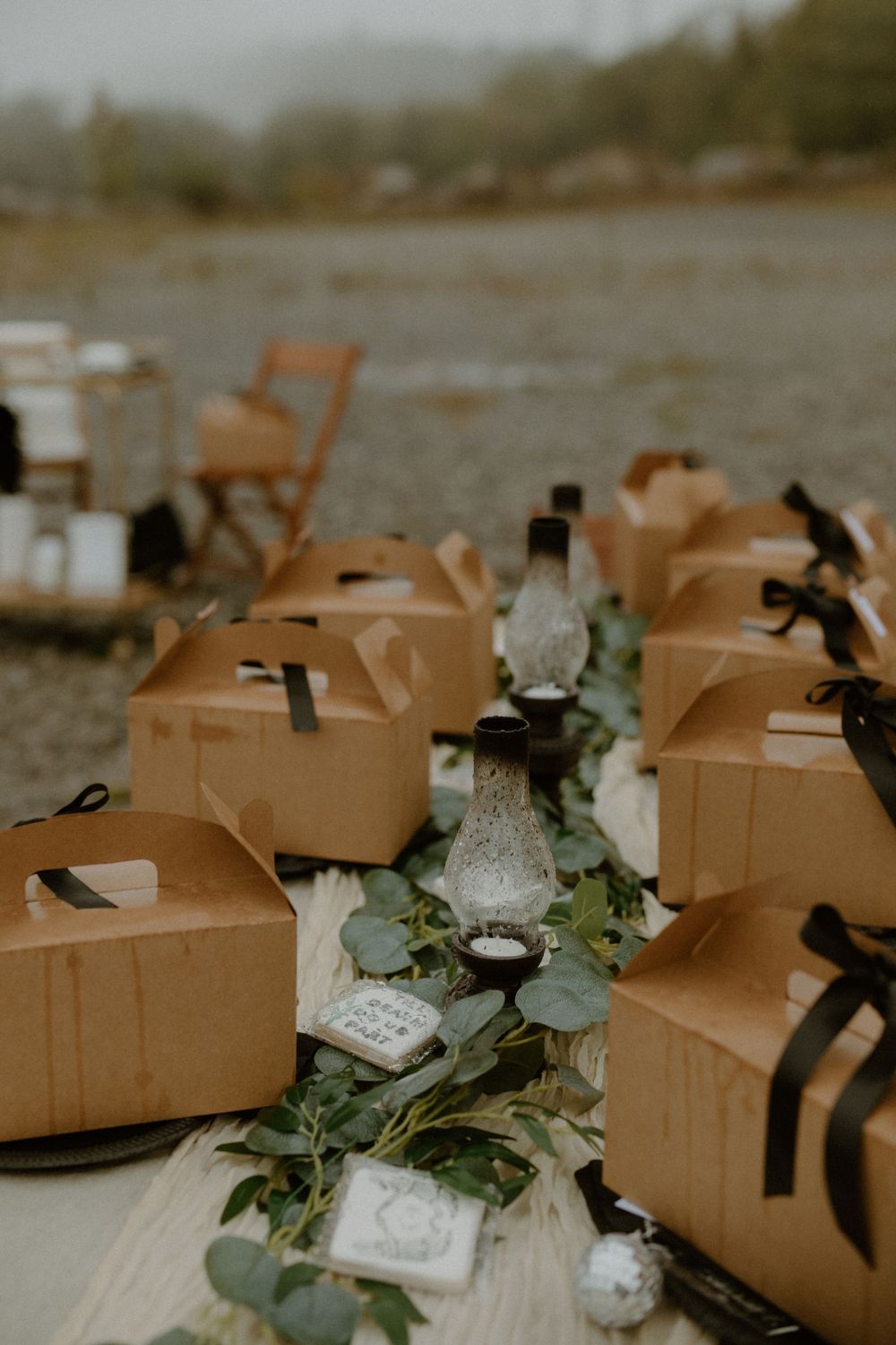 Kraft box wedding favors tied with black ribbon arranged on a table with eucalyptus greenery.