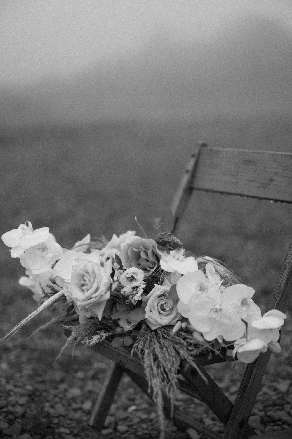 Black and white bridal bouquet of roses on wooden chair in fog.