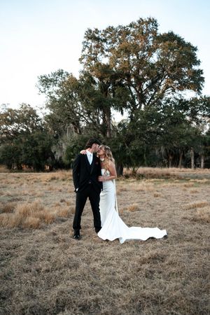 Bride and groom share a romantic moment in a rustic field with large oak trees during their outdoor wedding ceremony.