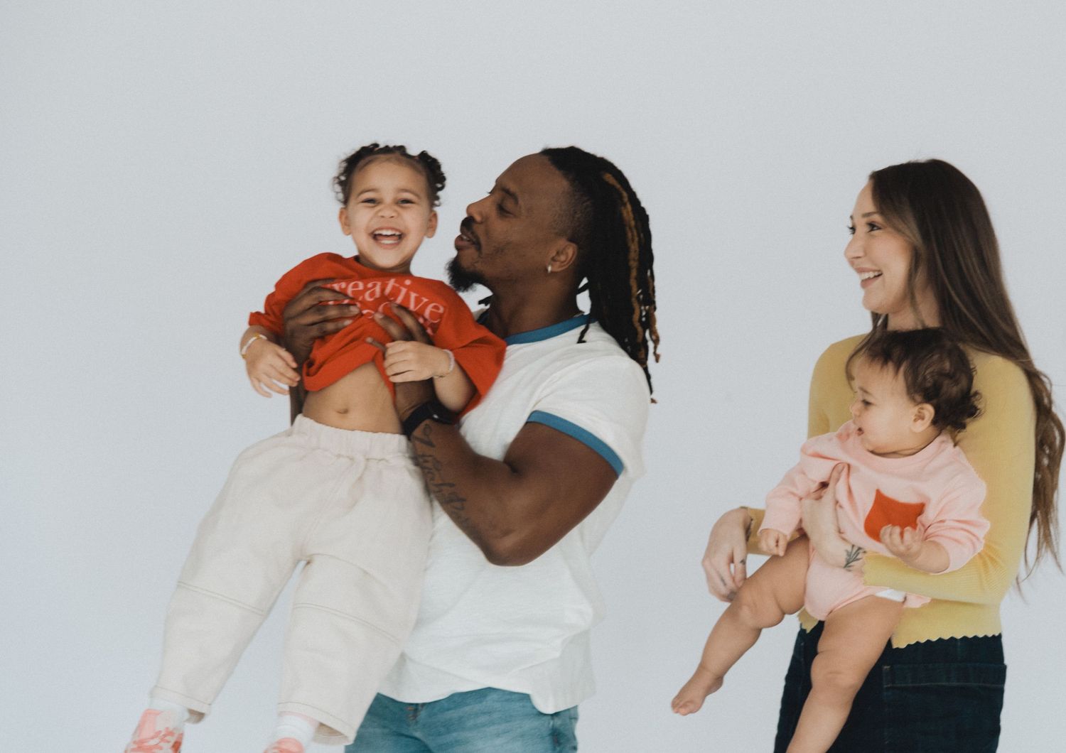 Happy interracial family with two young children smiling and laughing together against a white background.