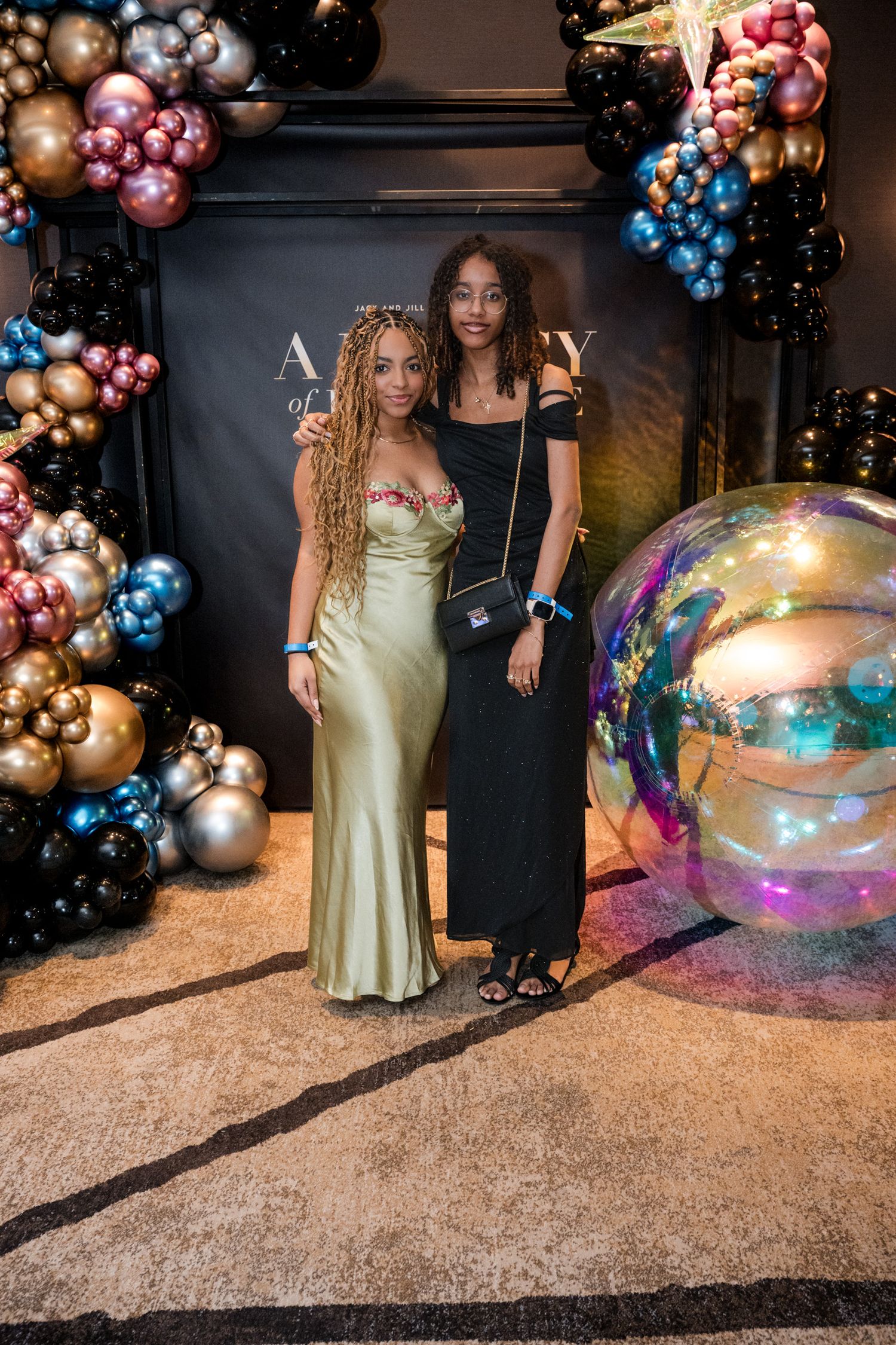 Two women posing together at elegant event with colorful balloon arch decoration backdrop.