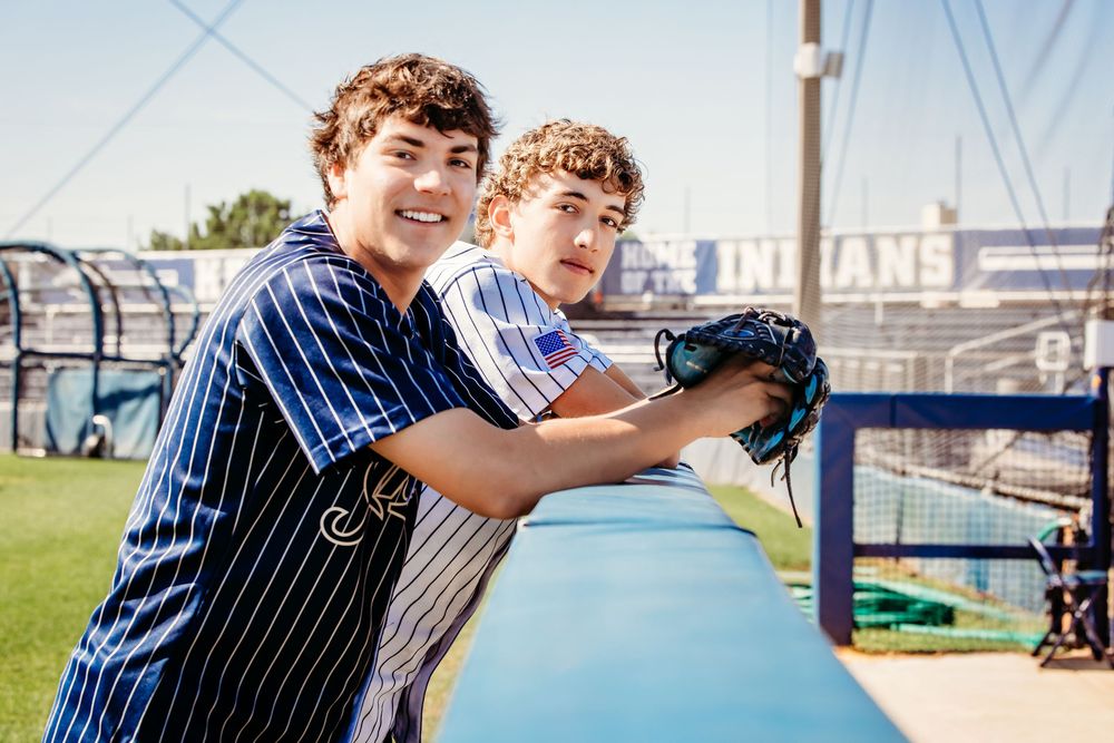 Two young baseball players in pinstripe uniforms lean on a dugout railing at an Indians baseball field in Keller, TX.
