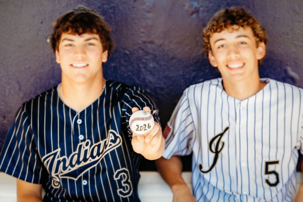 Two teenage baseball players in pinstripe uniforms holding a baseball outdoors in Keller, TX.