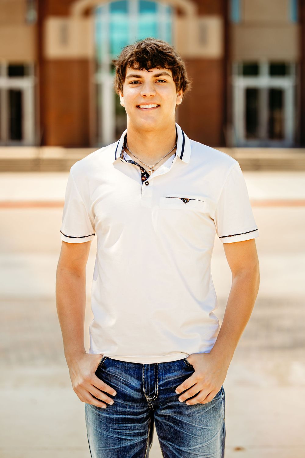 Smiling young man in white polo shirt and jeans standing outdoors in front of Keller Town Hall building in Keller, TX.
