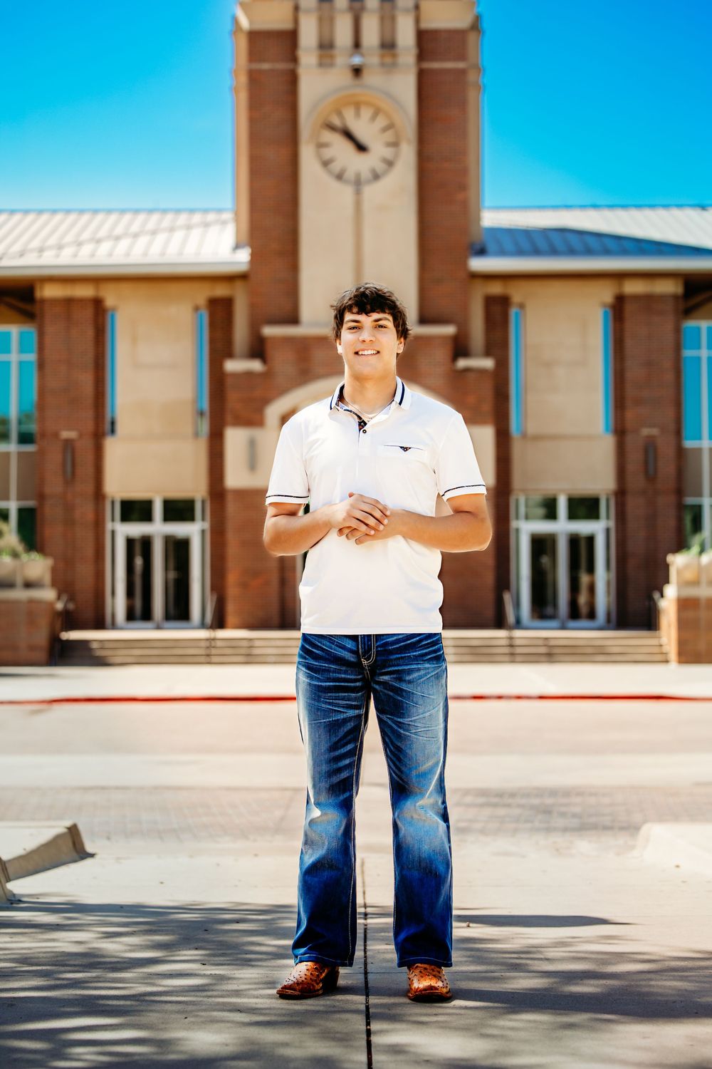 Young man in white polo and jeans smiling in front of a Keller Town Hall building in Keller, TX.