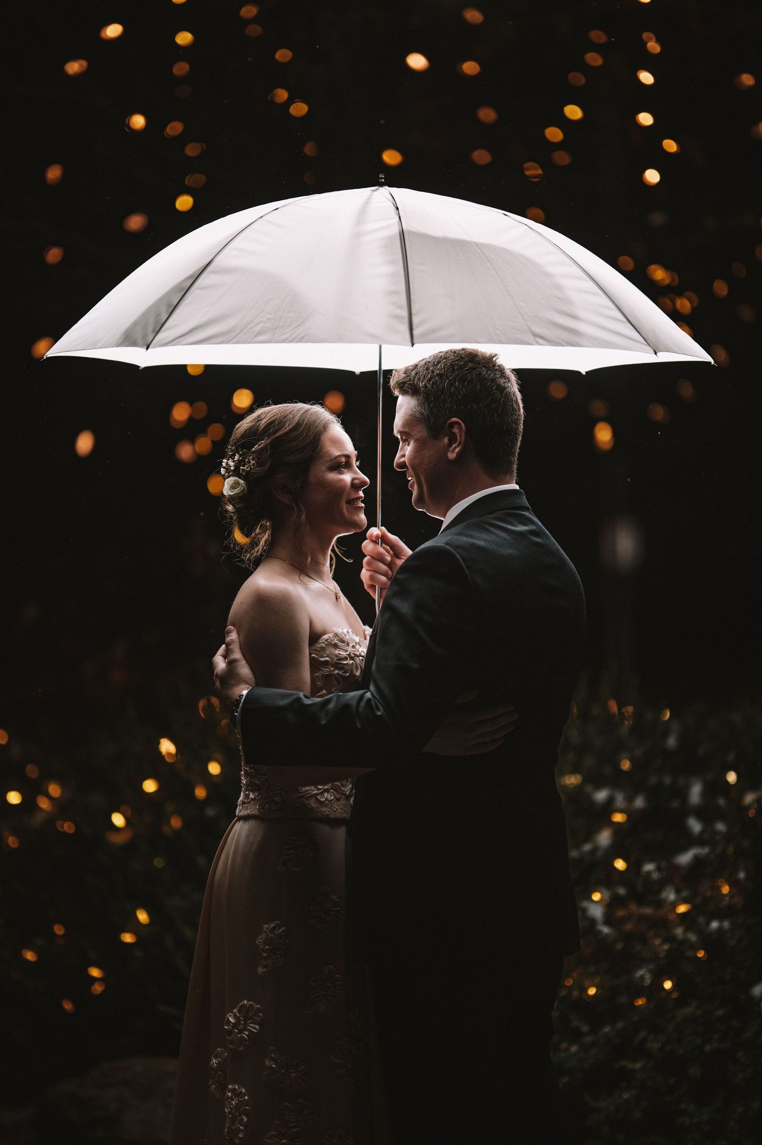 Romantic silhouette of couple with white umbrellas against bokeh light background.