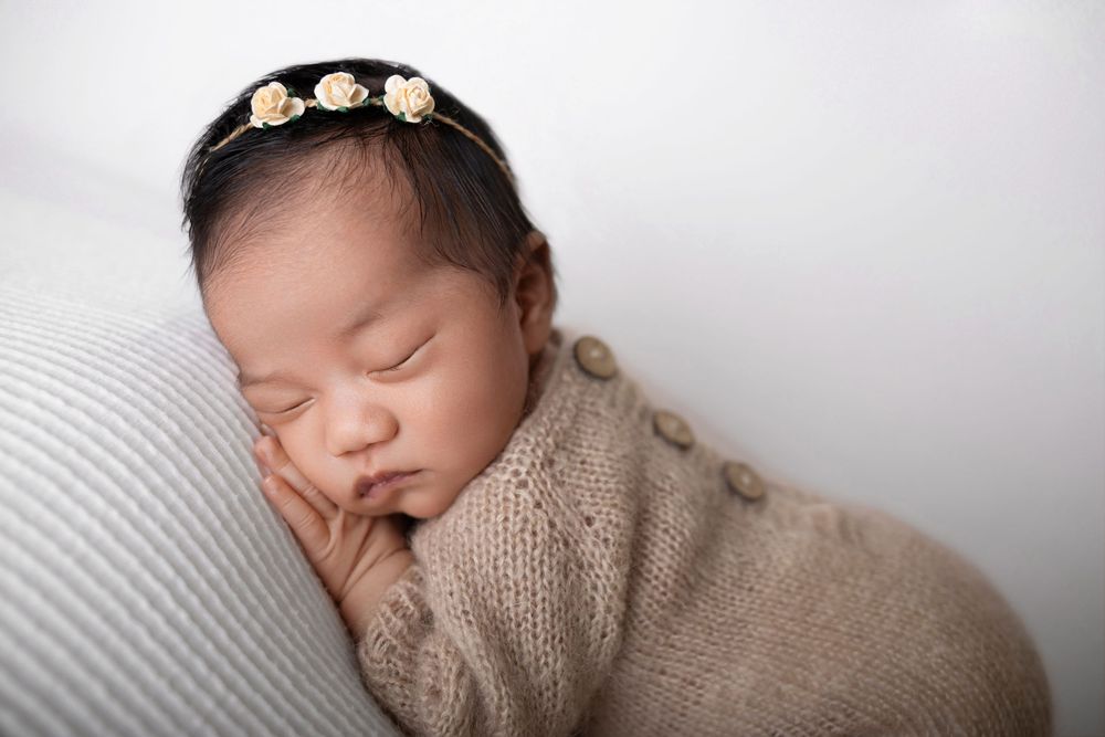 Sleeping newborn baby girl wrapped in a beige knit swaddle wearing a delicate floral headband. NJ studio photographer in Morris County NJ
