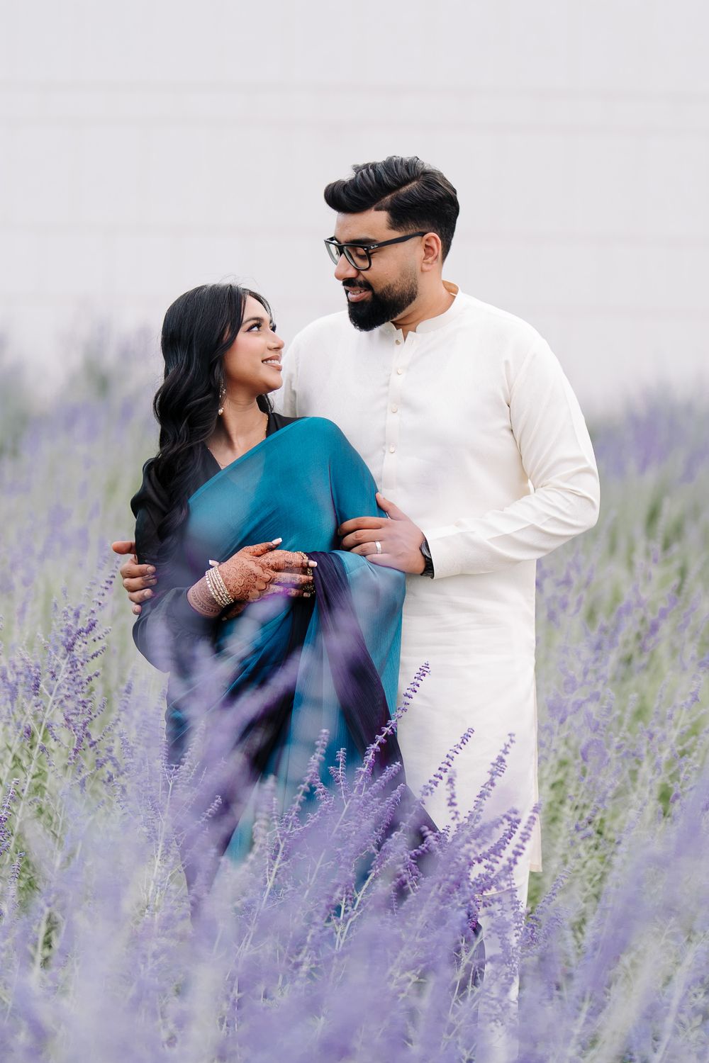A couple in traditional South Asian attire embraces in a blooming lavender field, sharing a romantic gaze.
