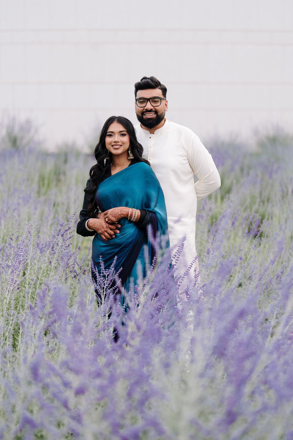 Couple in traditional Indian attire posing in a purple lavender field, woman in teal saree and man in white kurta.
