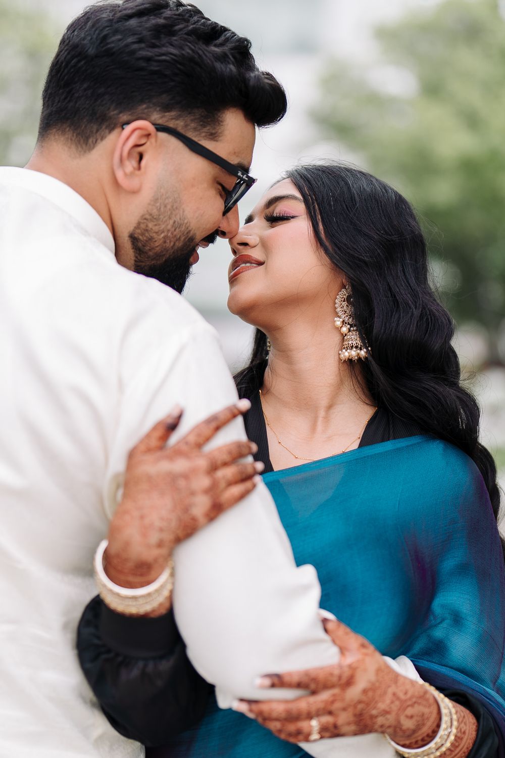 Indian couple in traditional attire sharing a romantic moment, woman in teal saree with gold jewelry, man in white kurta.