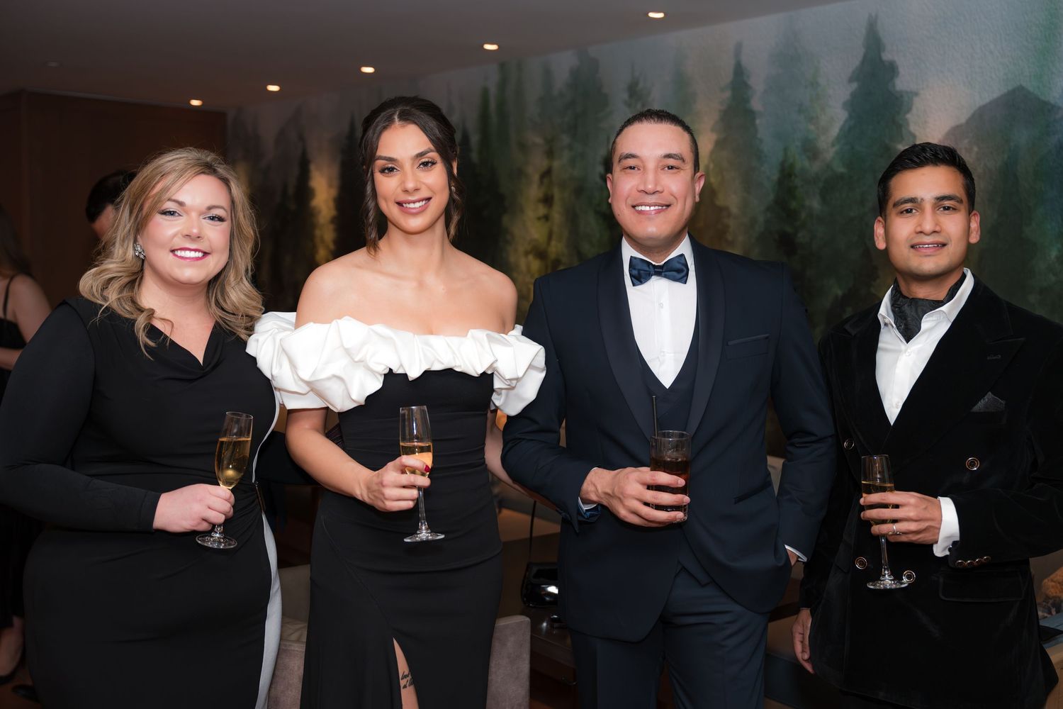 Four elegantly dressed guests holding champagne glasses pose together at a formal evening event.