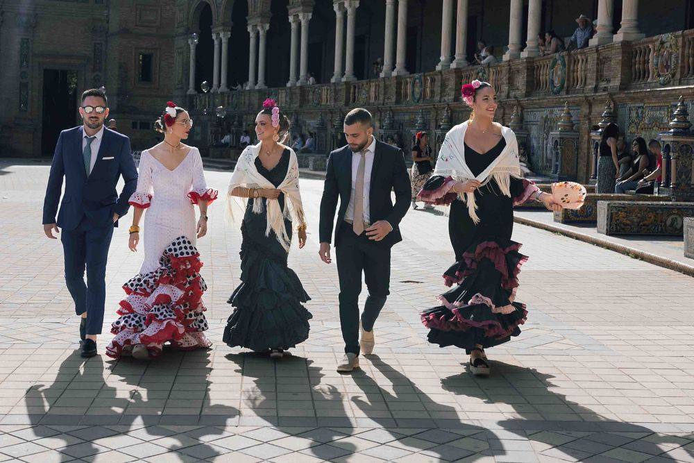 Group of five people in traditional Spanish flamenco attire walking at Plaza de España, Seville, Spain.
