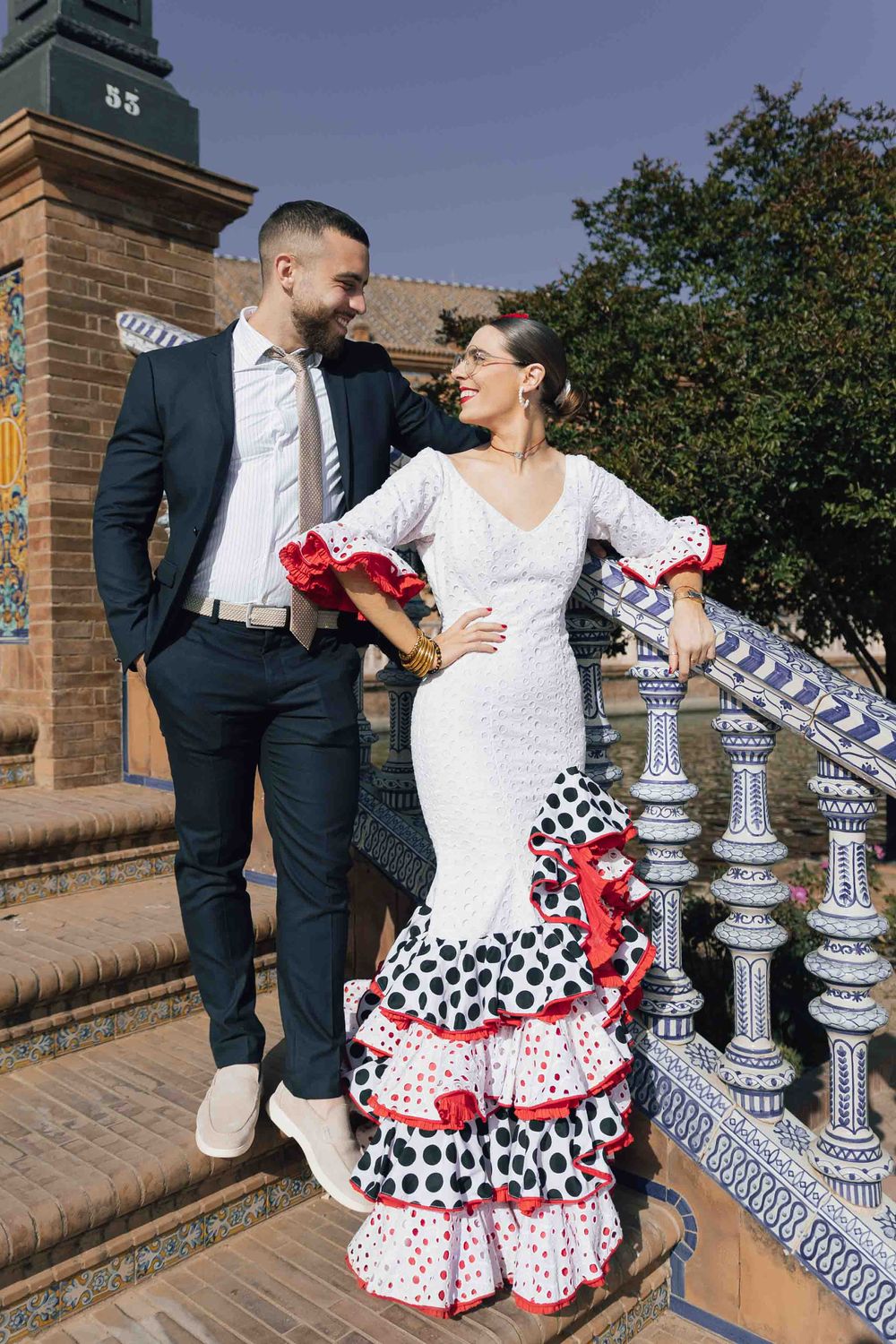 Couple in traditional flamenco attire posing on ornate tiled steps at Plaza de España, Seville, Spain.