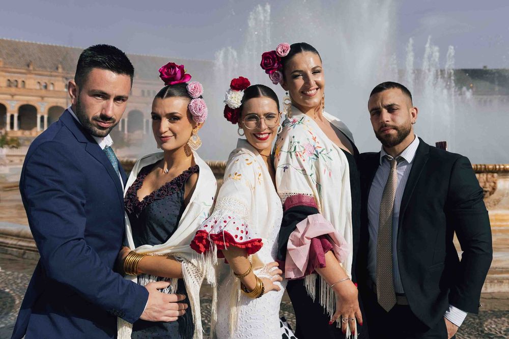 Group of five people in traditional Spanish flamenco attire posing at Plaza de España in Seville, Spain.