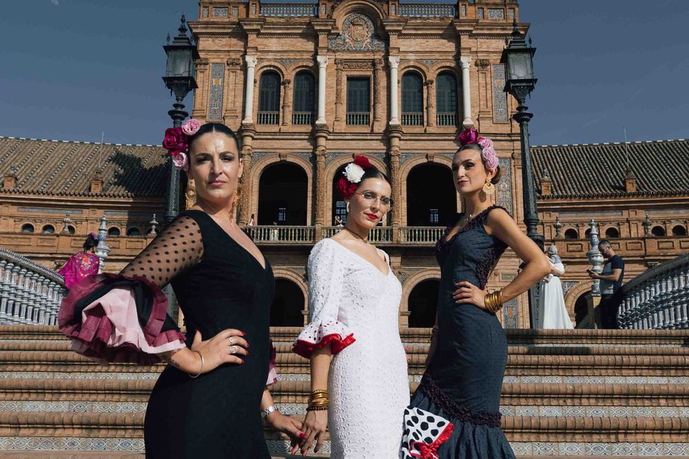 Three women in traditional Spanish flamenco dresses pose at Plaza de España in Seville, Spain.
