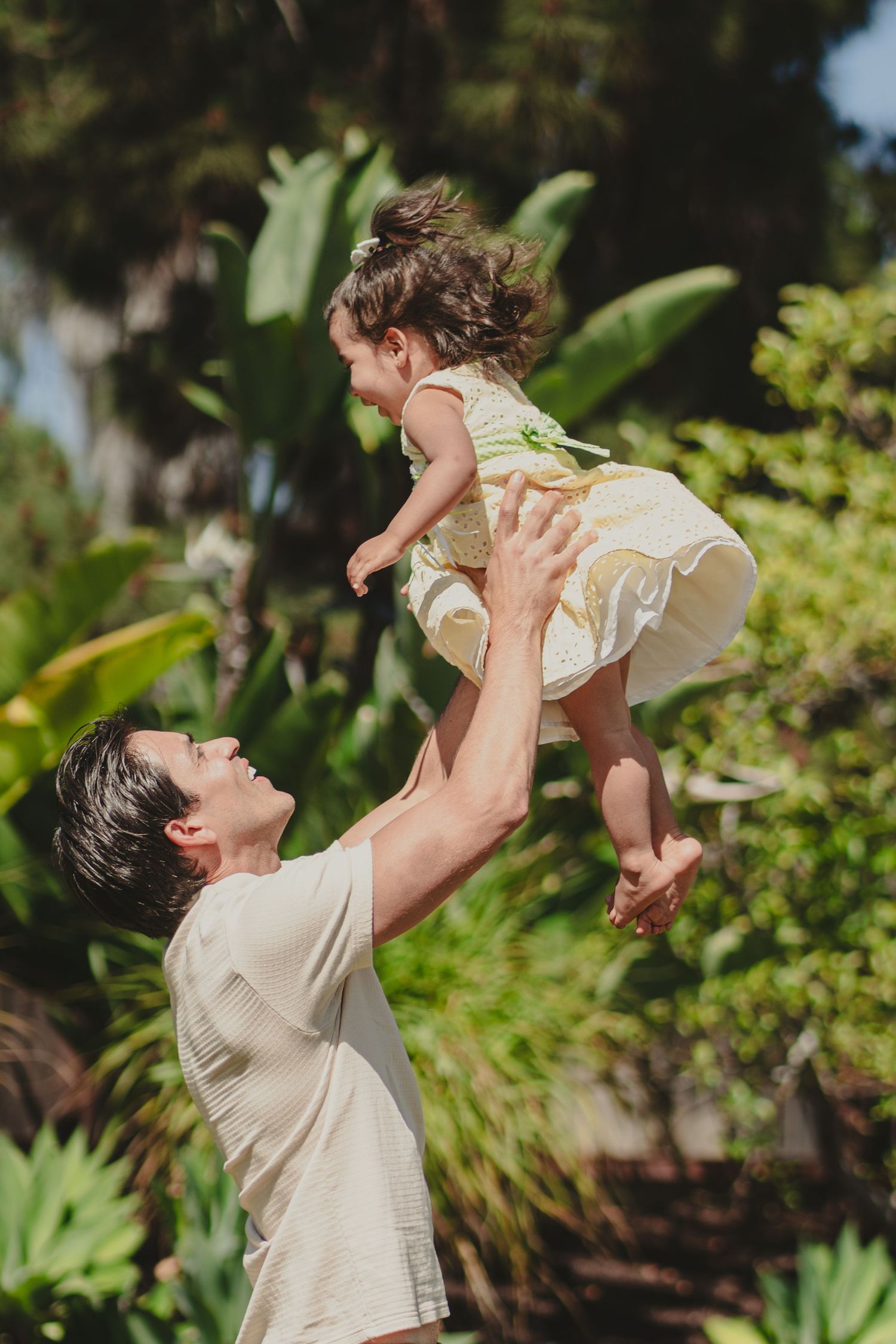 Father tossing up his daughter with tropical plants in the background. Encinitas, CA