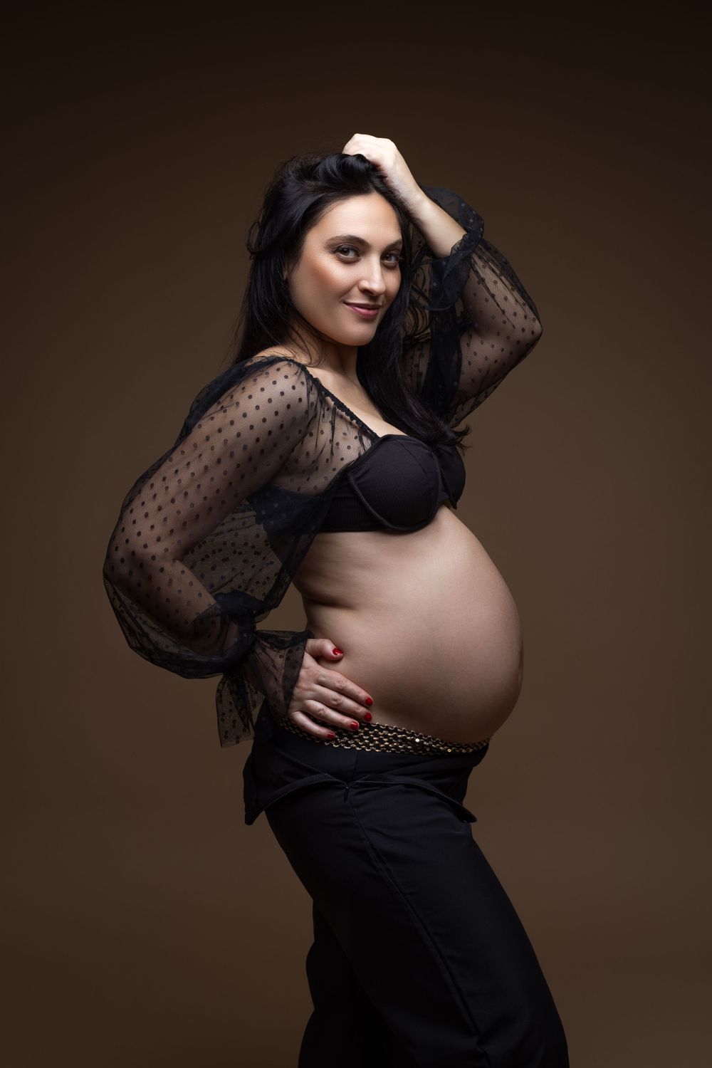 Maternity portrait showing pregnant woman in black lace top against dark background.
