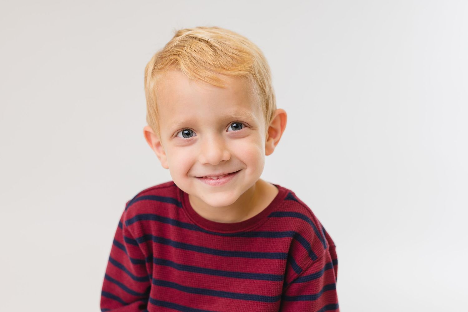 Child wearing a red sweater and hair bows poses for a close-up portrait.