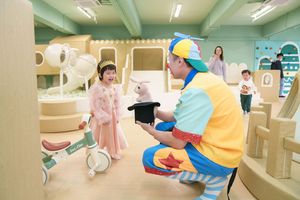 A clown performs a magic trick with a rabbit in a hat for a delighted child at a colorful indoor play area.
