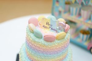 Pastel rainbow birthday cake with macarons and a topper reading Paris Happy 3rd Birthday.
