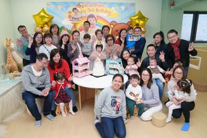 Large group of family and friends celebrating a child's 1st birthday party with cakes and colorful decorations.