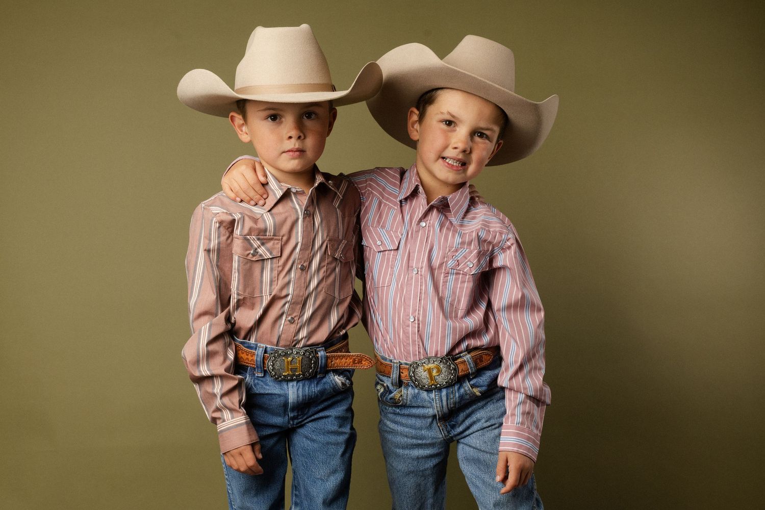 Two young boys in matching cowboy hats and striped western shirts posing together for a portrait.