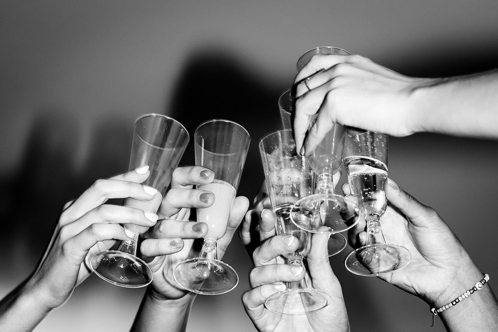 Black and white photo of multiple hands clinking champagne glasses together in a celebratory toast.