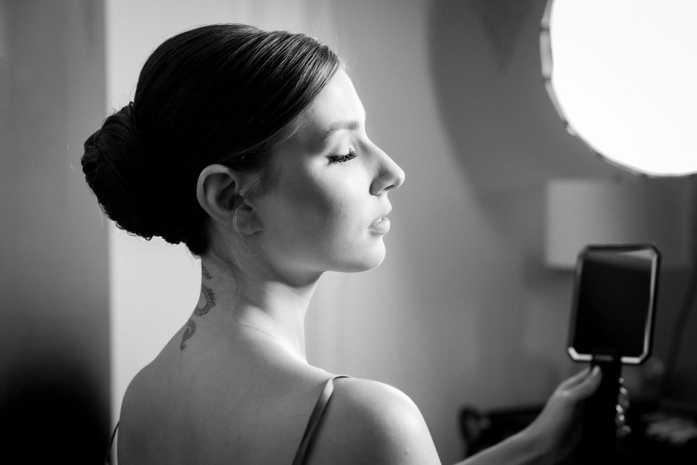 Black and white portrait of a young woman with elegant updo hairstyle posing gracefully beside a round studio light.