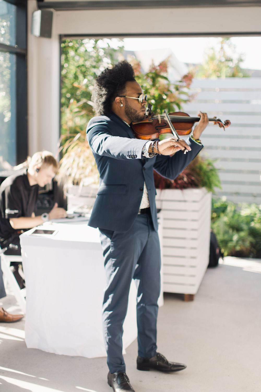 A Black male violinist in a blue suit performs at an elegant indoor event with bright natural lighting.