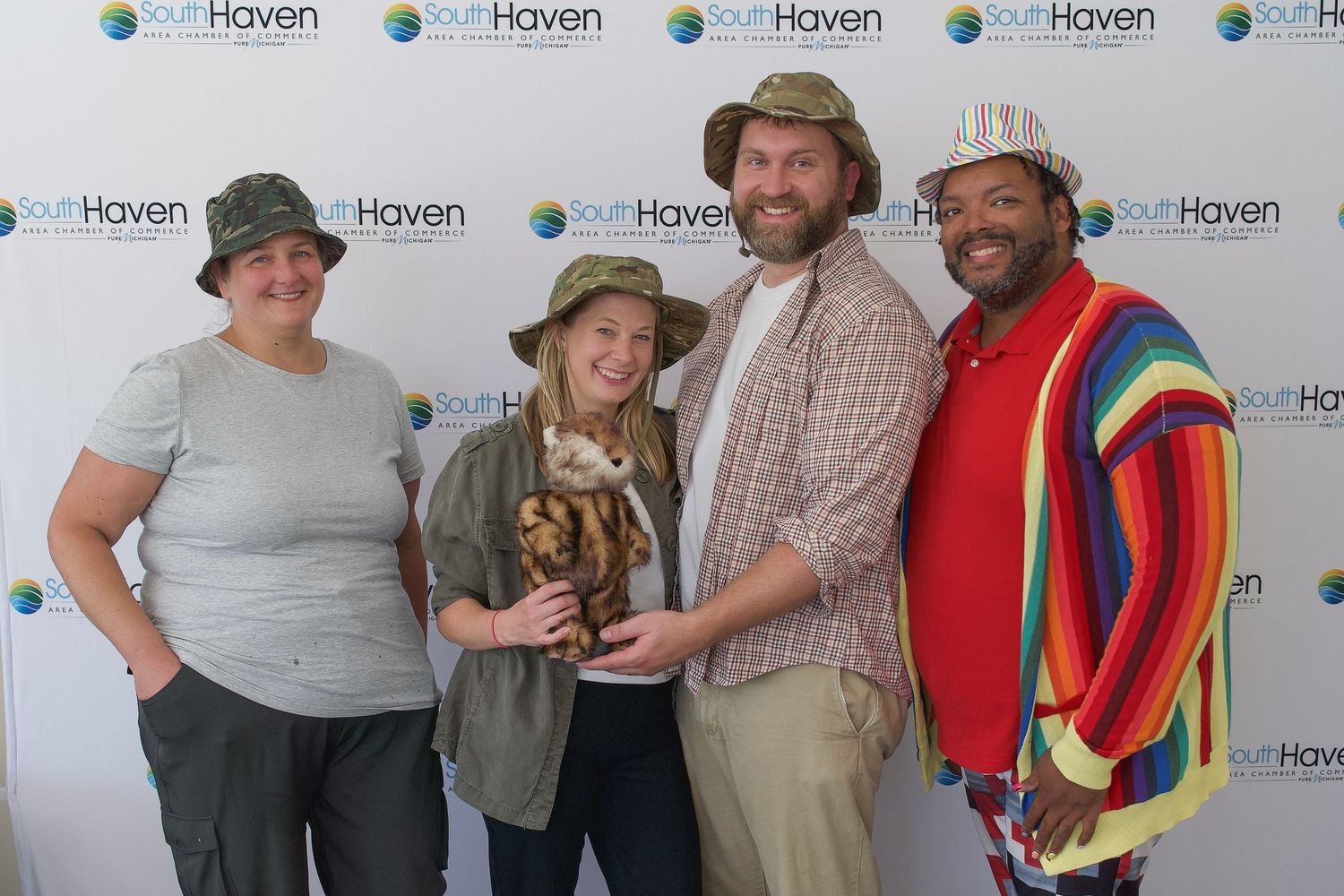 Four people posing together at a South Haven event, one holding a tiger trophy, dressed in colorful safari-themed outfits.