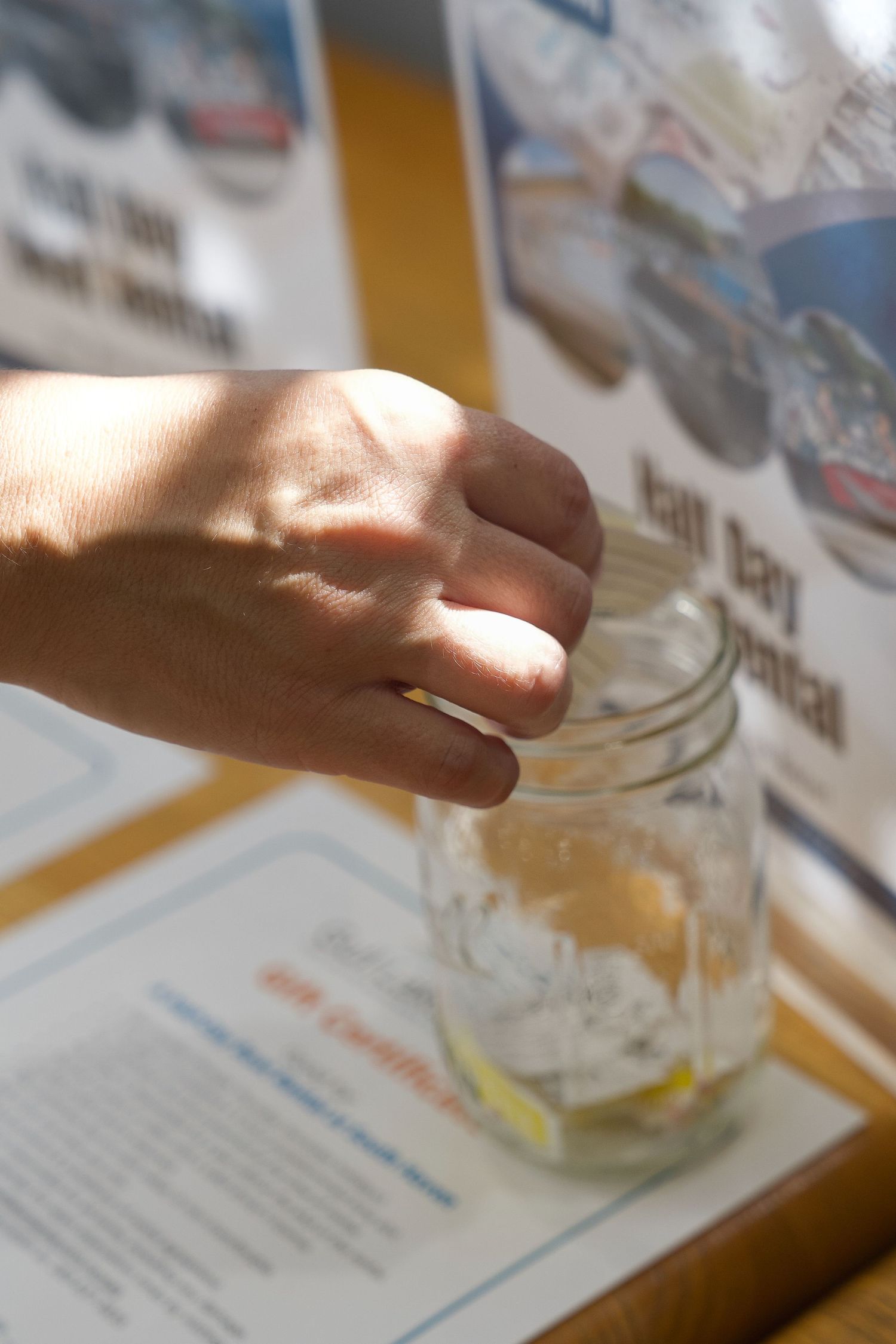 A hand reaching into a glass mason jar on a table with blurred documents and photos in the background.
