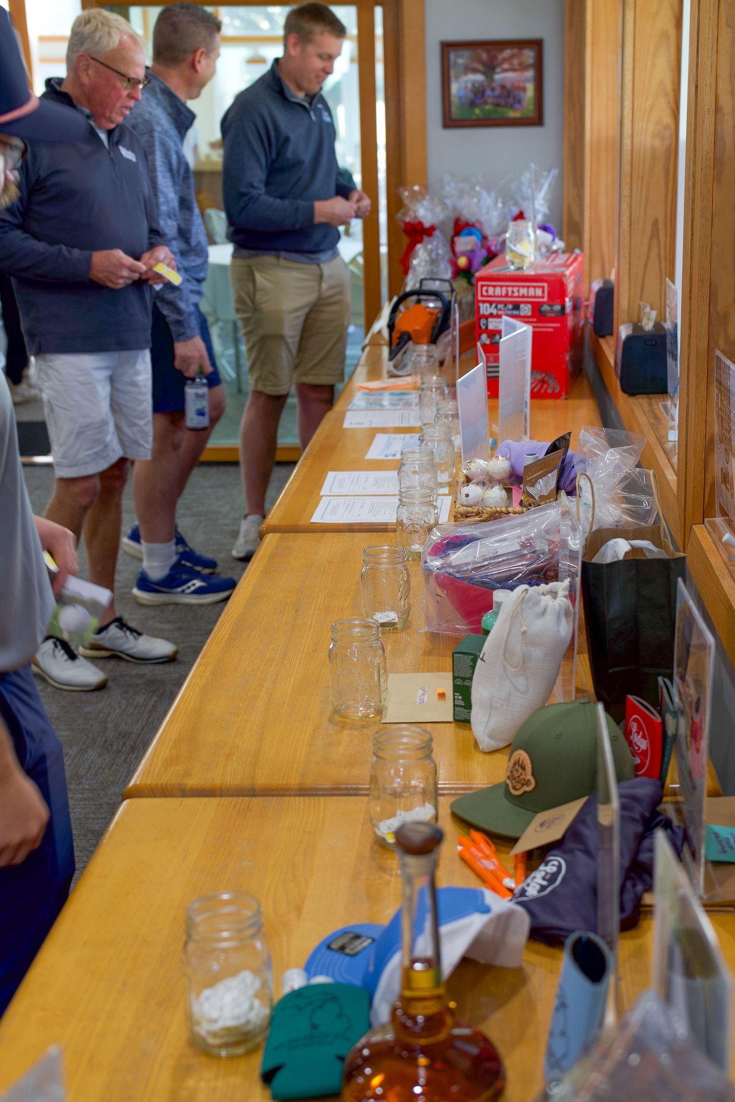 Silent auction table displays prizes including Craftsman tools, hats, and gift baskets at a golf event.