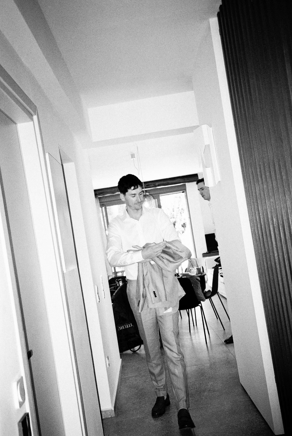 Black and white photo of a young man in a white shirt holding a jacket in a modern hallway.