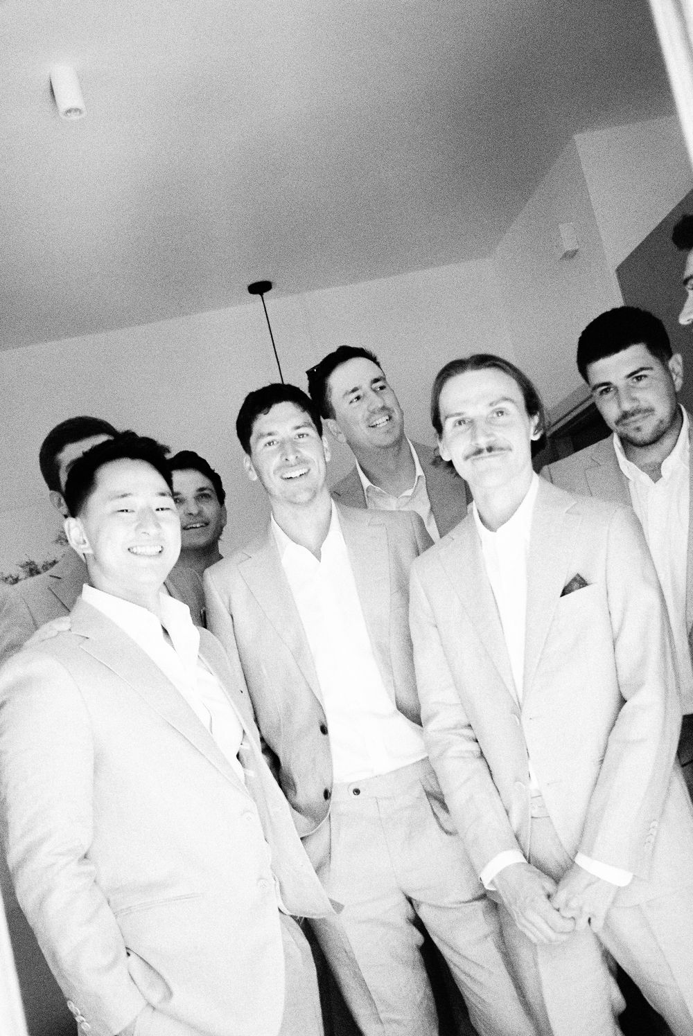 Black and white photo of a group of well-dressed men in suits smiling together at a formal event.